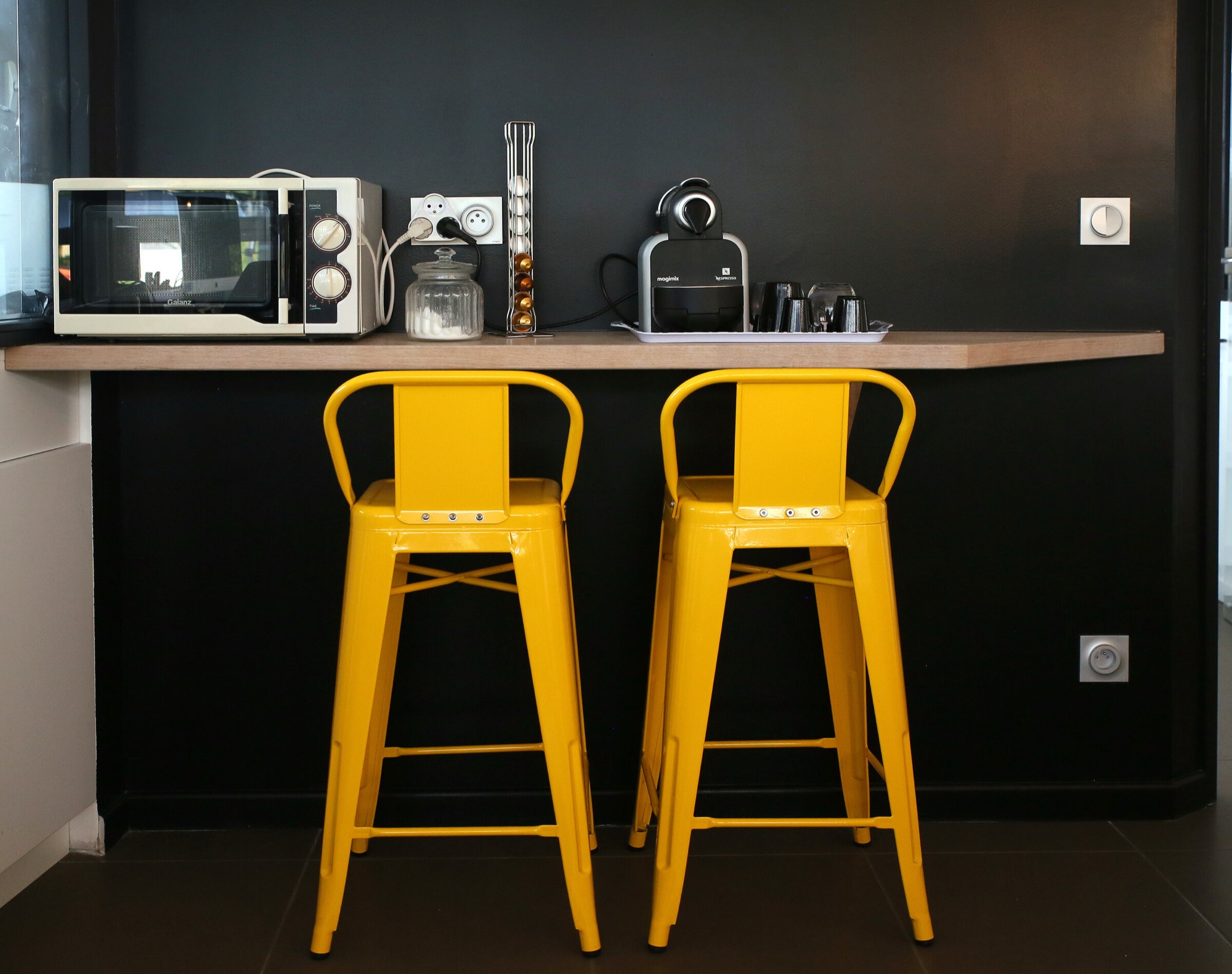 Agence de communication, bureaux — espace détente : plan de travail en bois et tabourets jaunes devant un mur noir