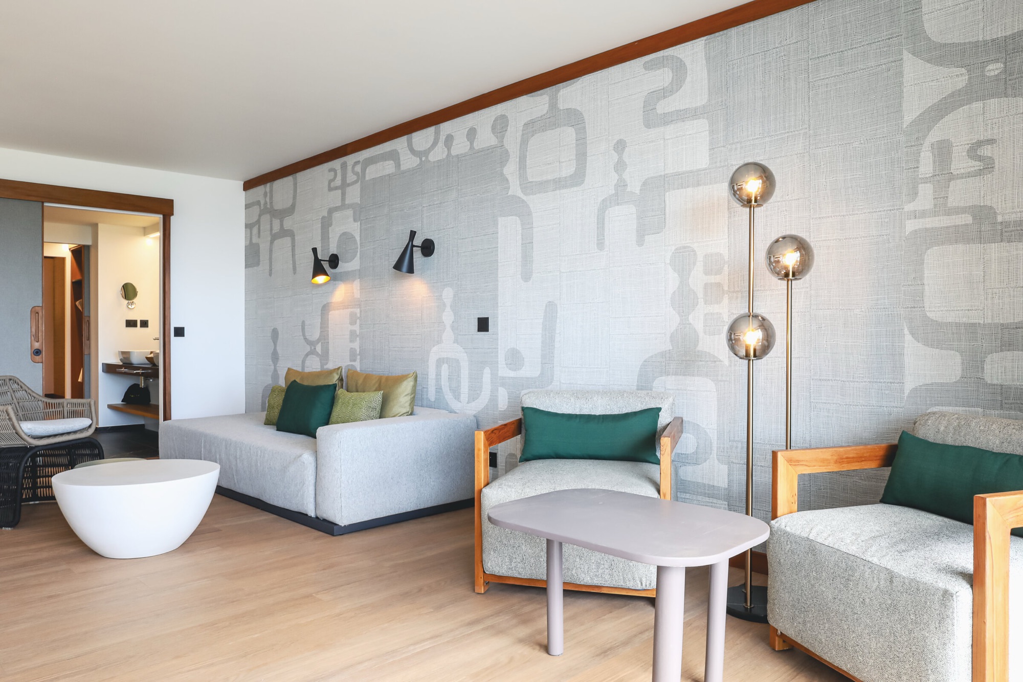 Hôtel Le Tahiti, Arue — suite : coin salon, canapé gris et fauteuils en bois devant la tapisserie murale sur mesure