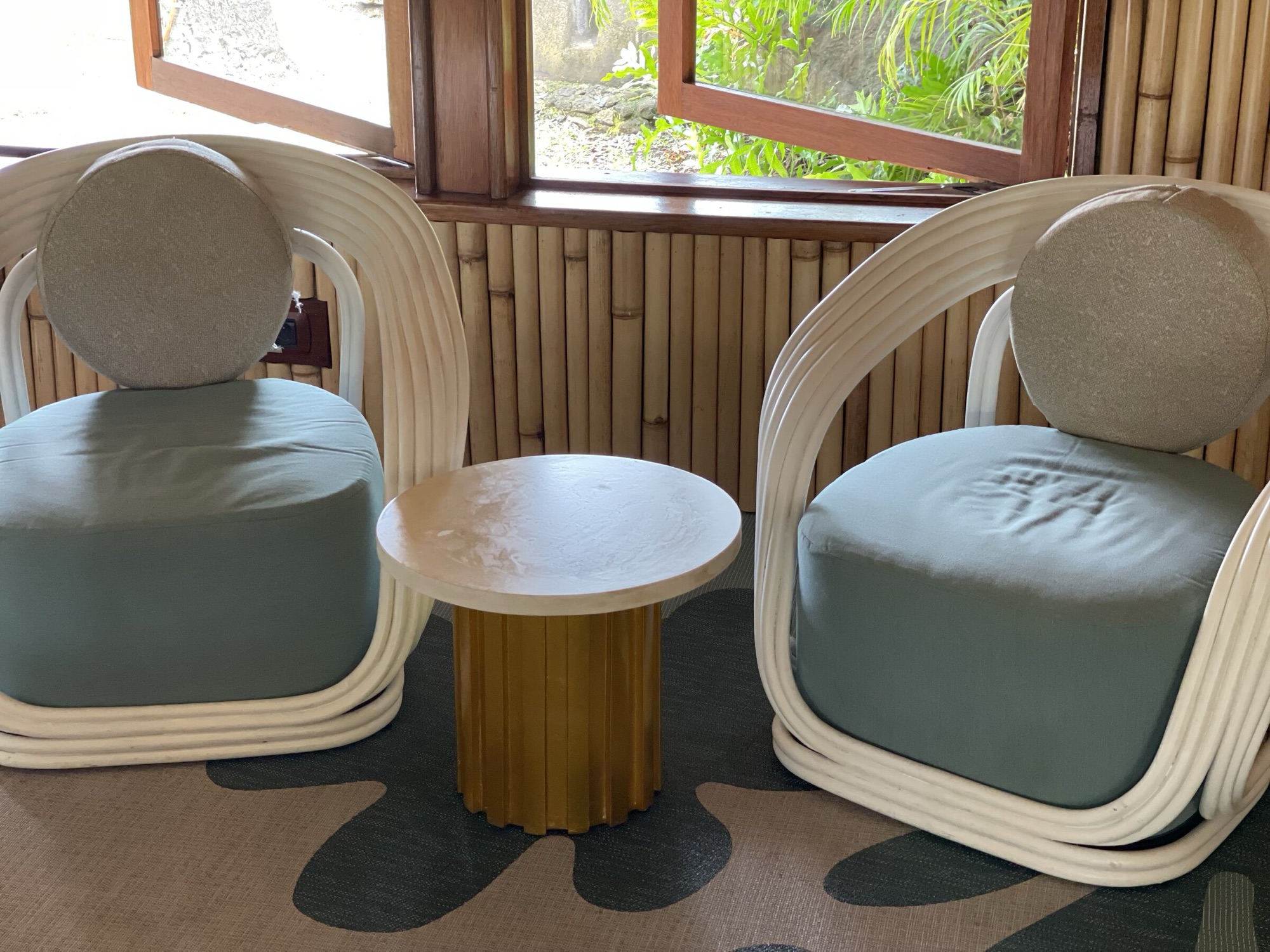 InterContinental Bora Bora, lobby — deux fauteuils en rotin blanc autour d'une table basse à piètement doré, devant les fenêtres sur le jardin