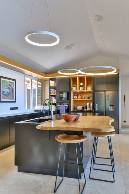 Maison particulière — cuisine : îlot sombre à plateau en bois brut et suspensions circulaires