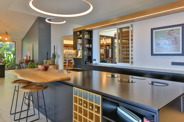 Maison particulière — cuisine : îlot en pierre sombre, plan de travail en bois brut et suspension circulaire